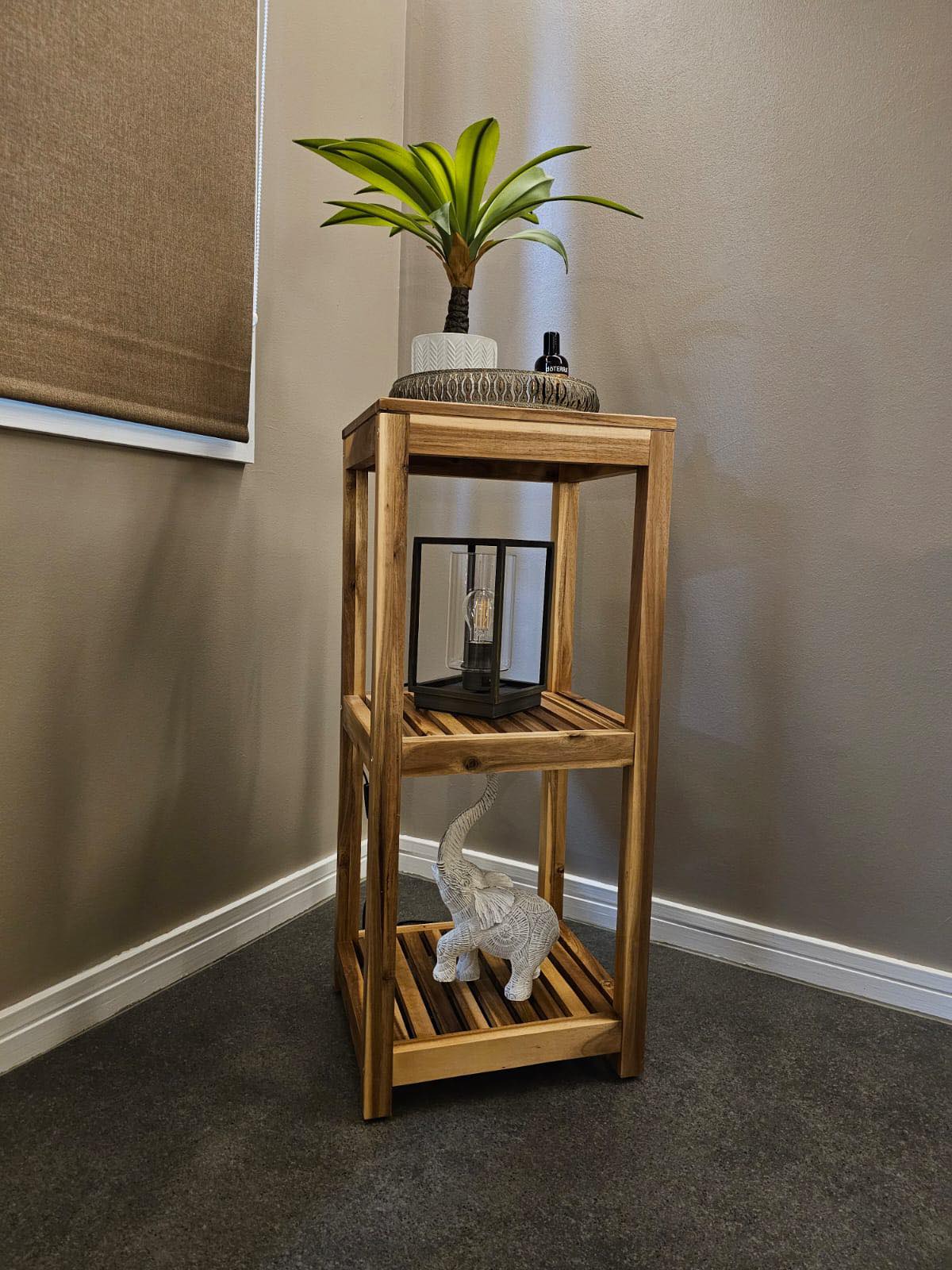 A wooden shelf unit in the corner of the room, with a lantern, a plant and an elephant ornament