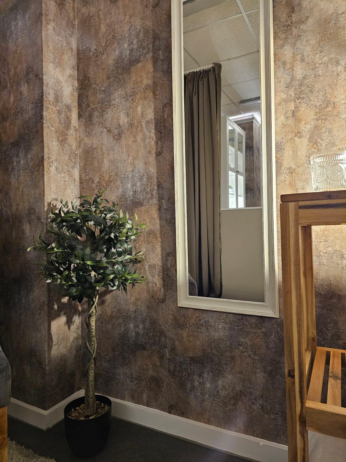 A tall mirror against the bronze feature wall, with a potted olive tree