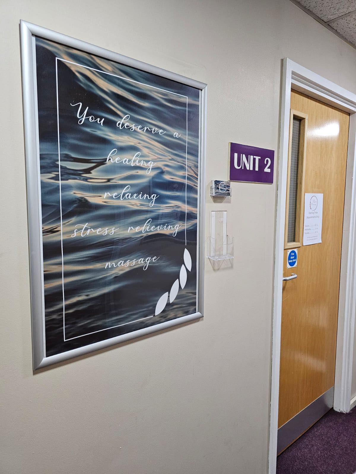 The corridor at the Flora Centre, with the Pure Massage poster beside the door marked Unit 2