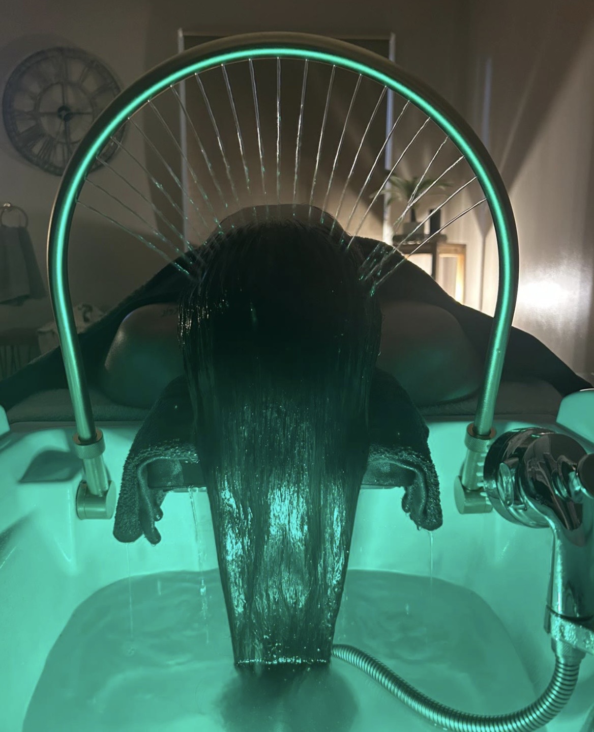 The head spa basin lit teal, with a client’s hair beneath the arched halo